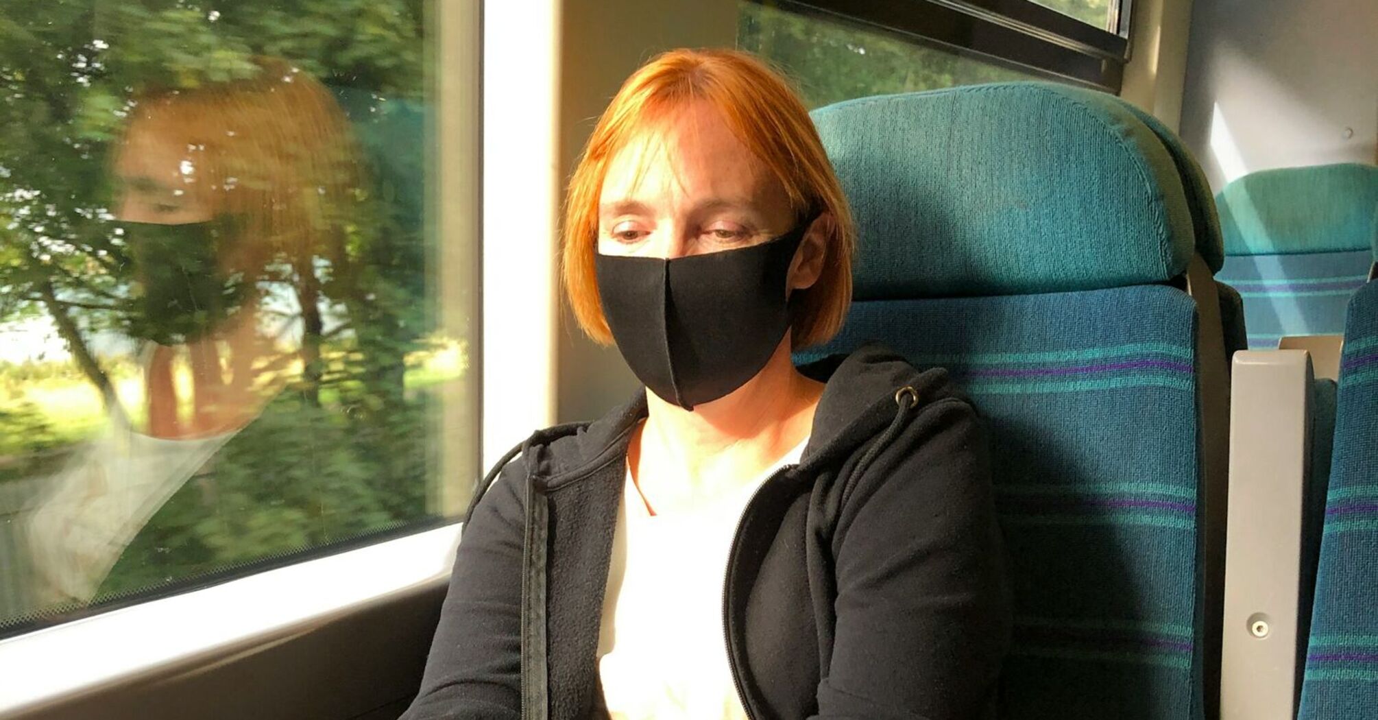 A woman wearing a black mask using her phone while traveling on a train