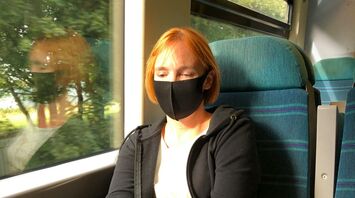 A woman wearing a black mask using her phone while traveling on a train