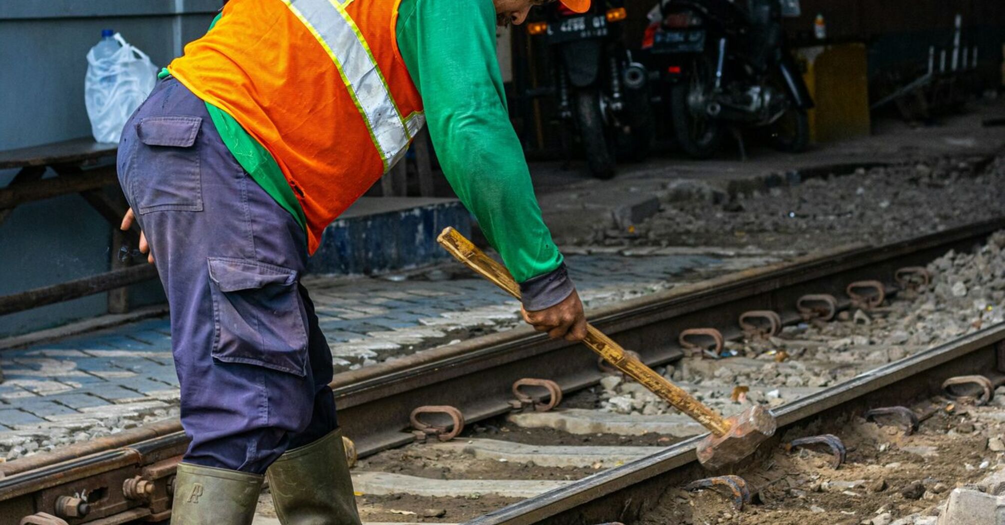 A railway worker in a high-visibility vest and helmet using tools to repair a track