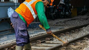 A railway worker in a high-visibility vest and helmet using tools to repair a track