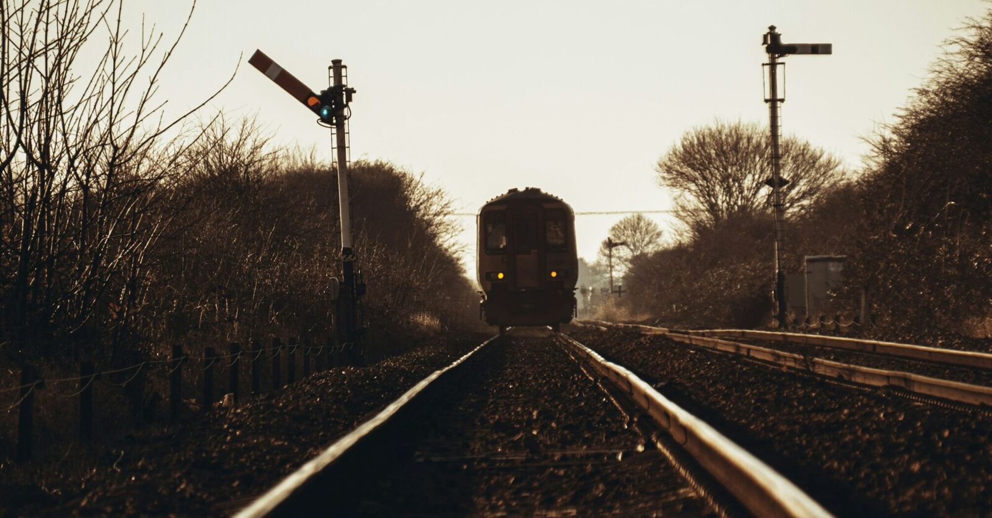 A train approaching on a railway track with signaling equipment visible, set against a background of bare trees under a clear sky in Skegness