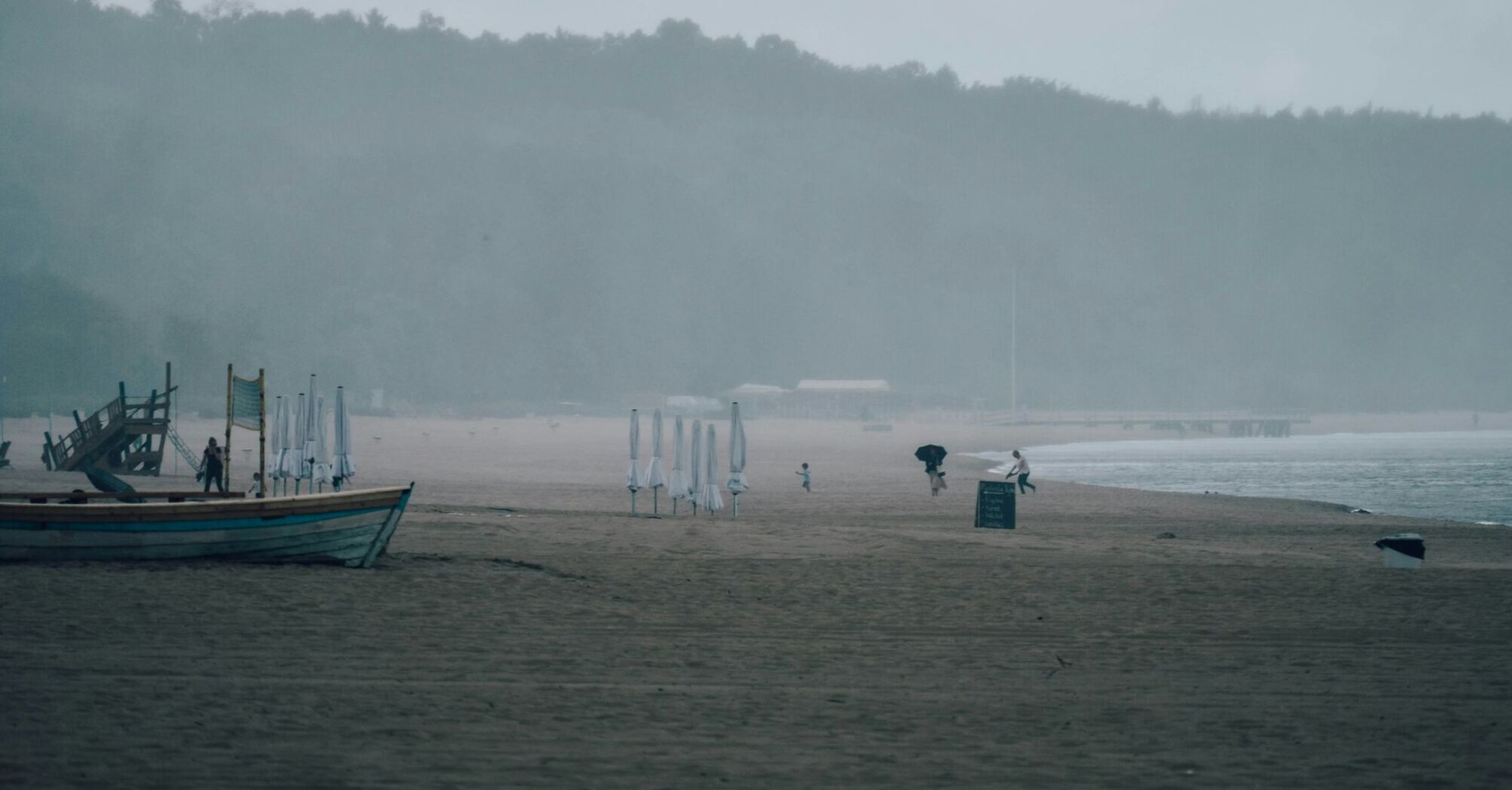 Empty beach with umbrellas and boats during rainy weather