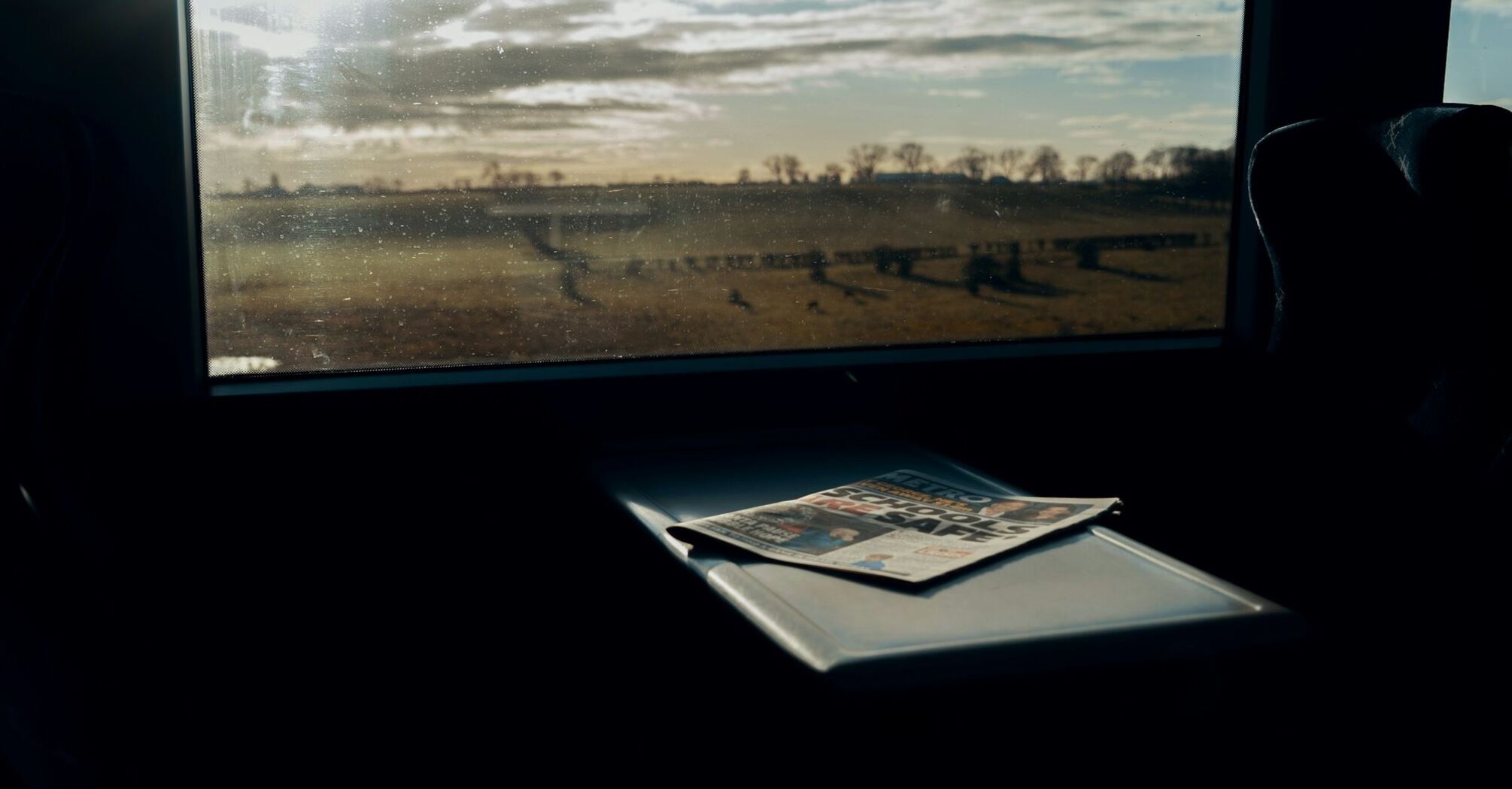 A scenic view through a train window with a newspaper on the table