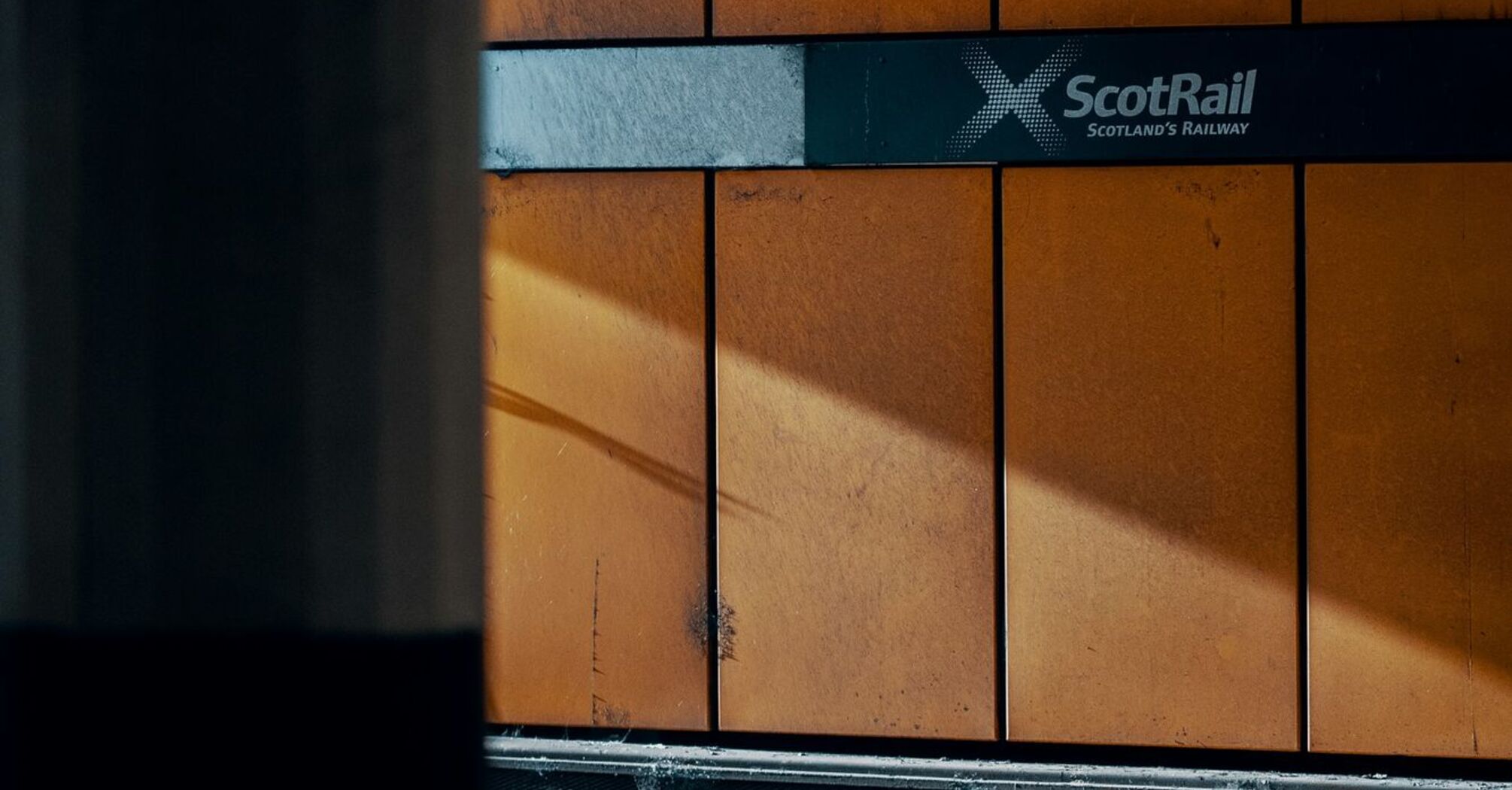 A ScotRail station platform with orange walls and the ScotRail logo