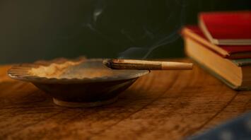 A burning incense stick in a metal holder with books