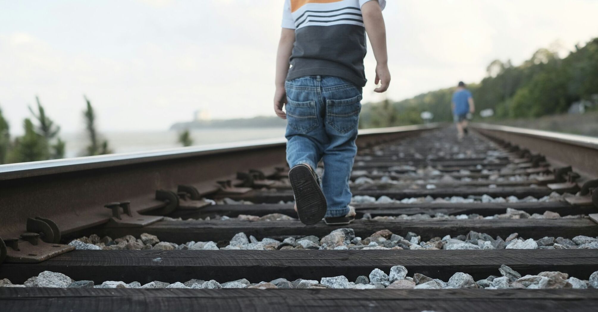 A child walking on railway tracks with an adult in the distance