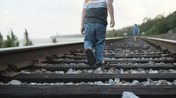 A child walking on railway tracks with an adult in the distance