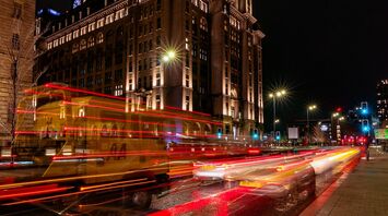 A bustling street in Liverpool at night with the iconic Liver Building in the background, illuminated by streetlights and passing vehicle lights