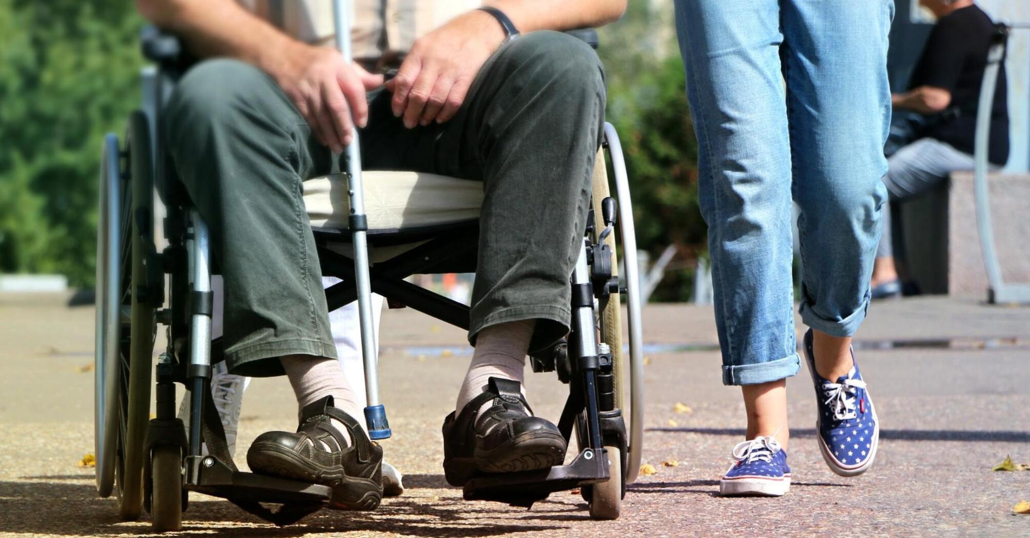 Elderly person in a wheelchair and accompanying person walking