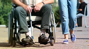 Elderly person in a wheelchair and accompanying person walking