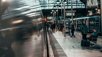 Passengers waiting at a train station platform under a glass roof