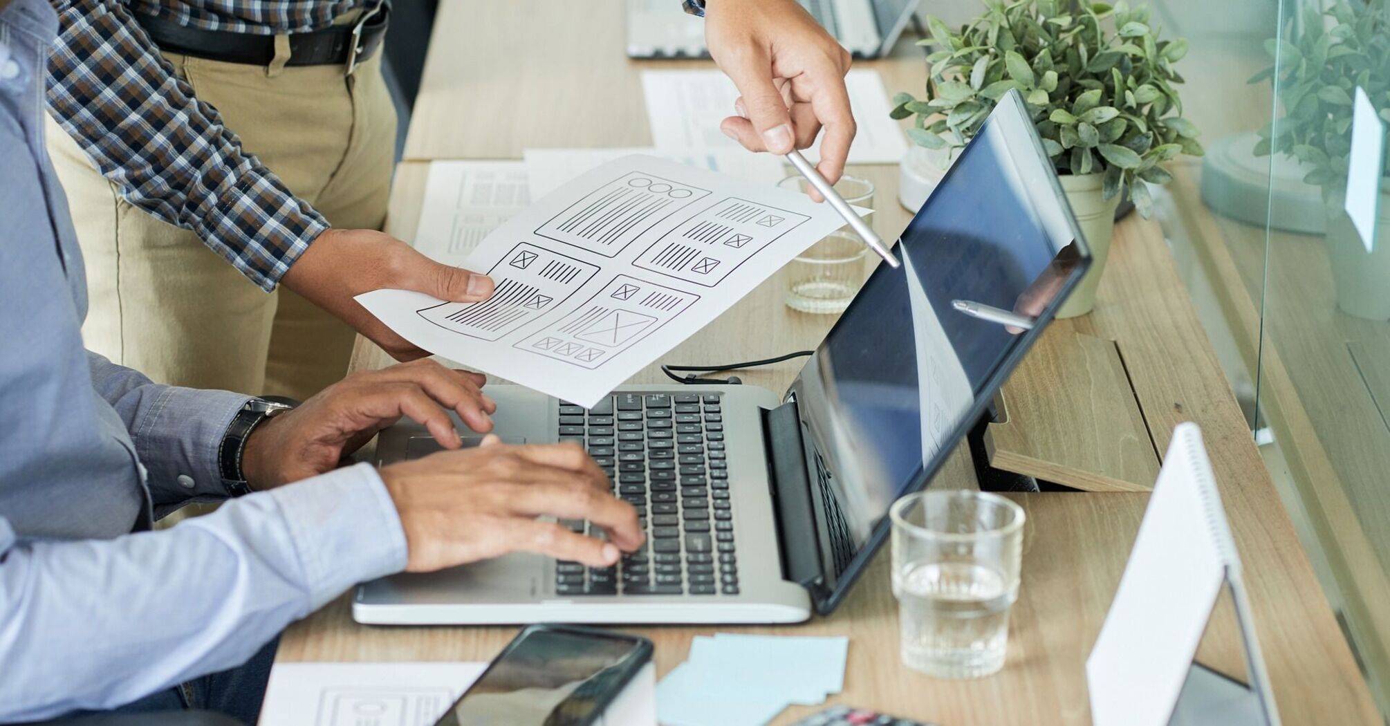 Two men working on a laptop with printed documents in an office