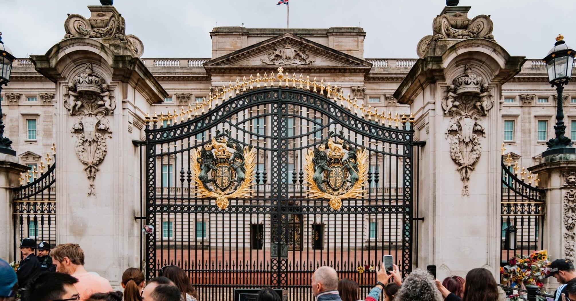 People in front of the gates of Buckingham Palace with the British flag