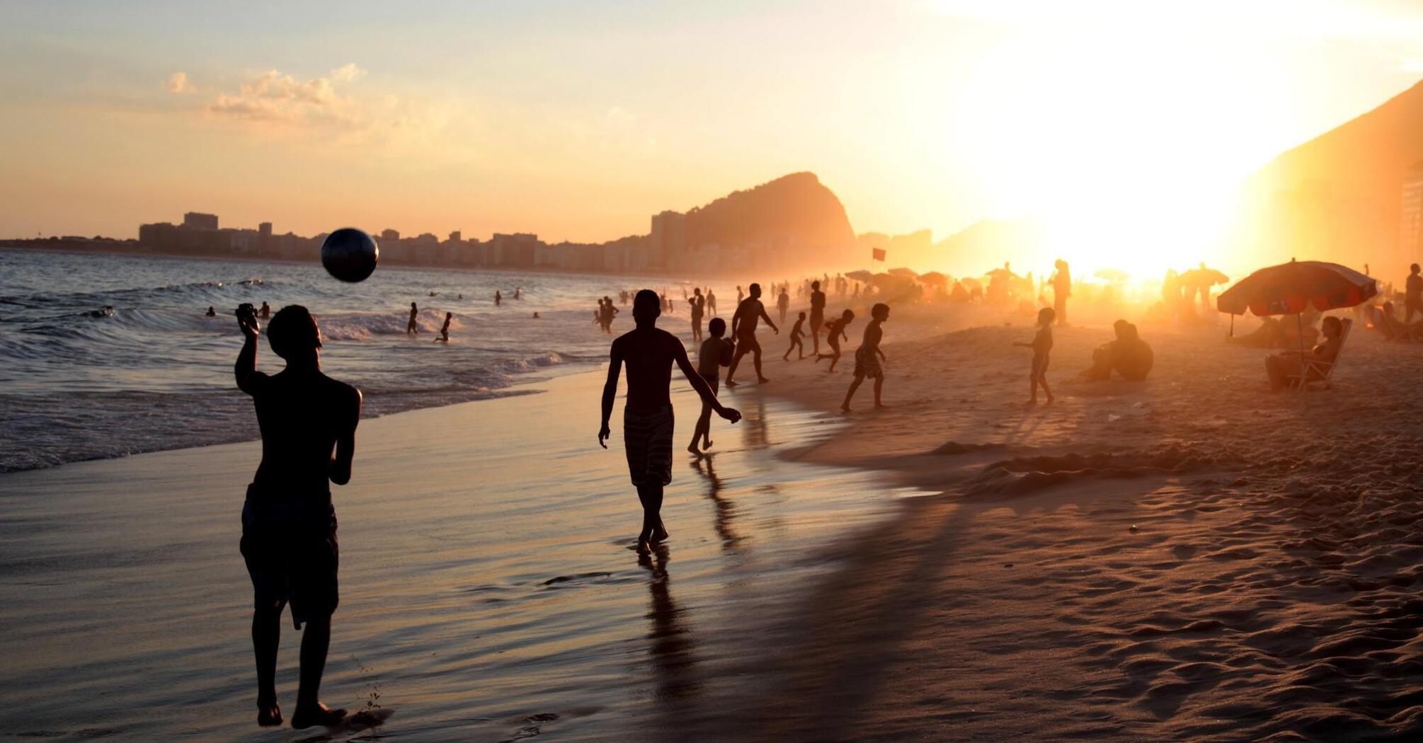 People playing beach soccer at sunset