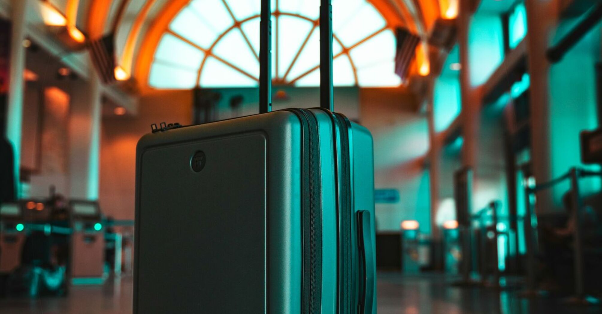 A modern suitcase stands in the middle of a brightly lit airport terminal with arched ceilings