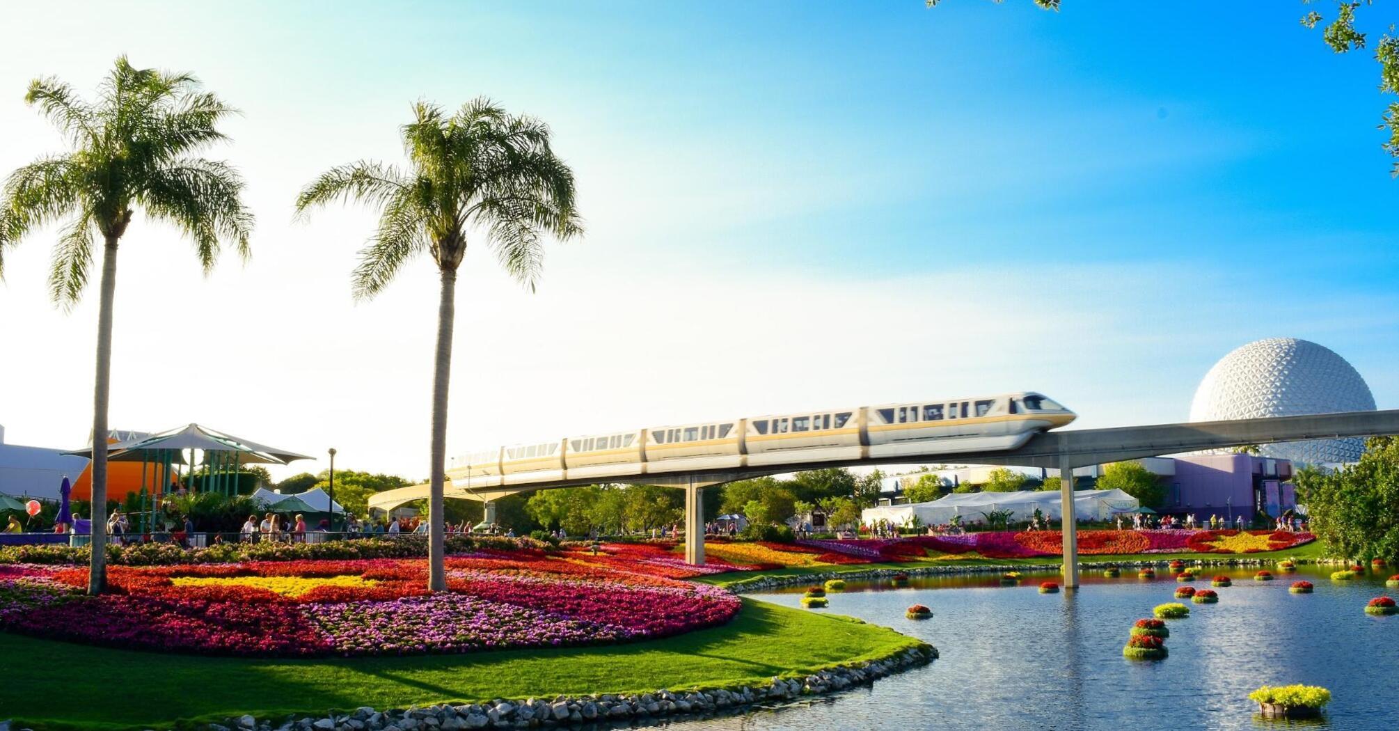 A view of a beautiful landscape with flower beds and a monorail passing through the park on a sunny day