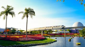 A view of a beautiful landscape with flower beds and a monorail passing through the park on a sunny day
