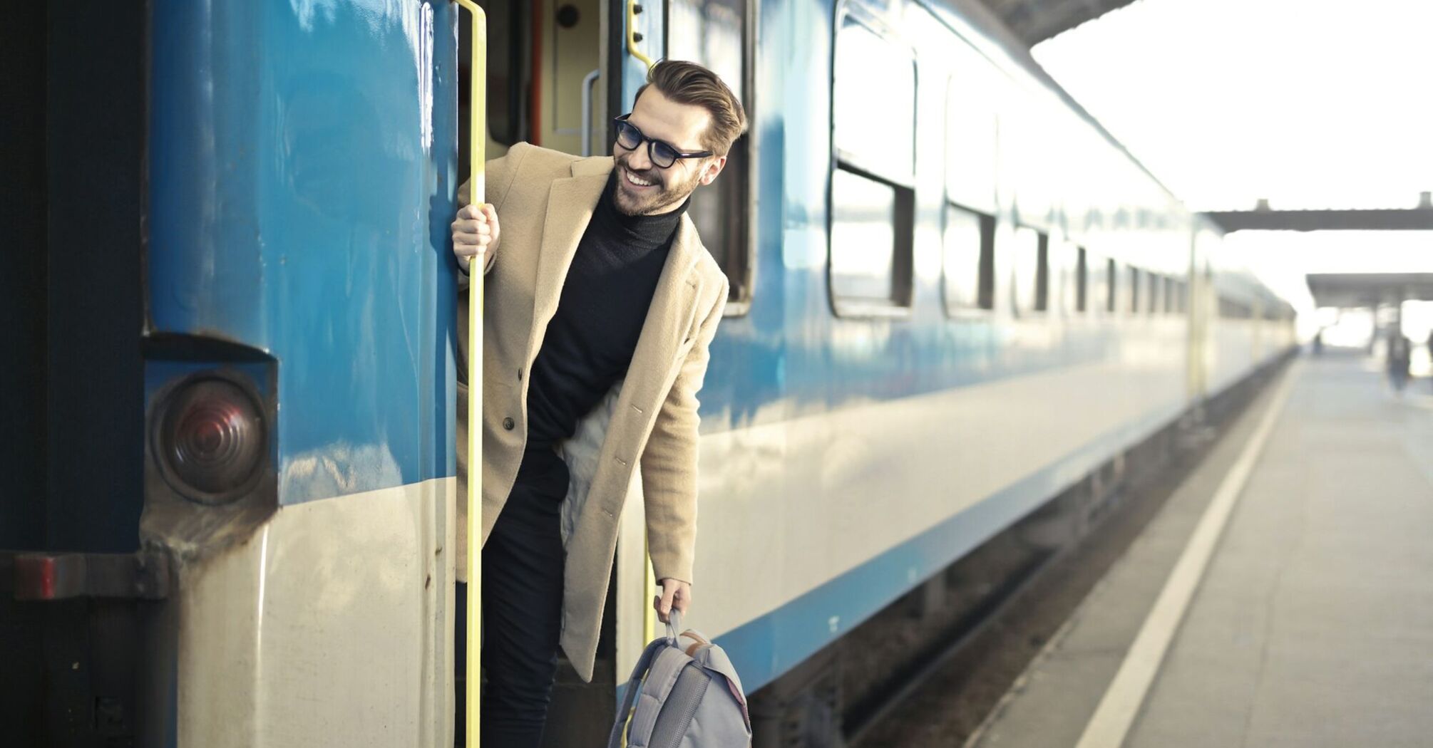 A man with a backpack stepping off a blue and white train at a station