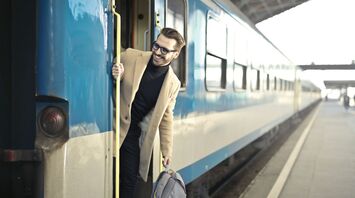 A man with a backpack stepping off a blue and white train at a station