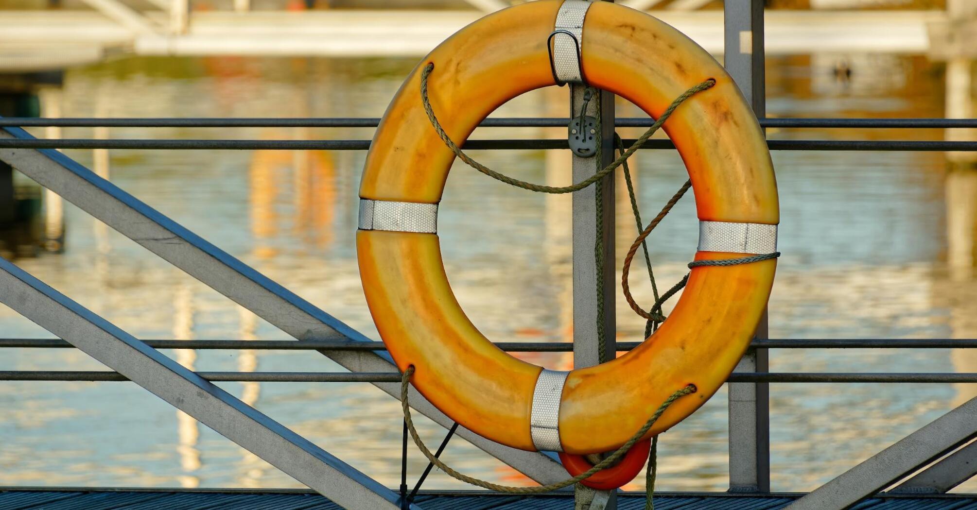 An orange lifebuoy hanging on a metal structure by the water