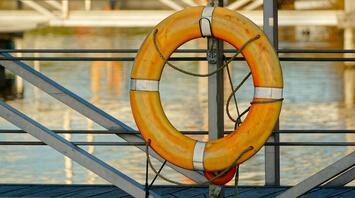 An orange lifebuoy hanging on a metal structure by the water
