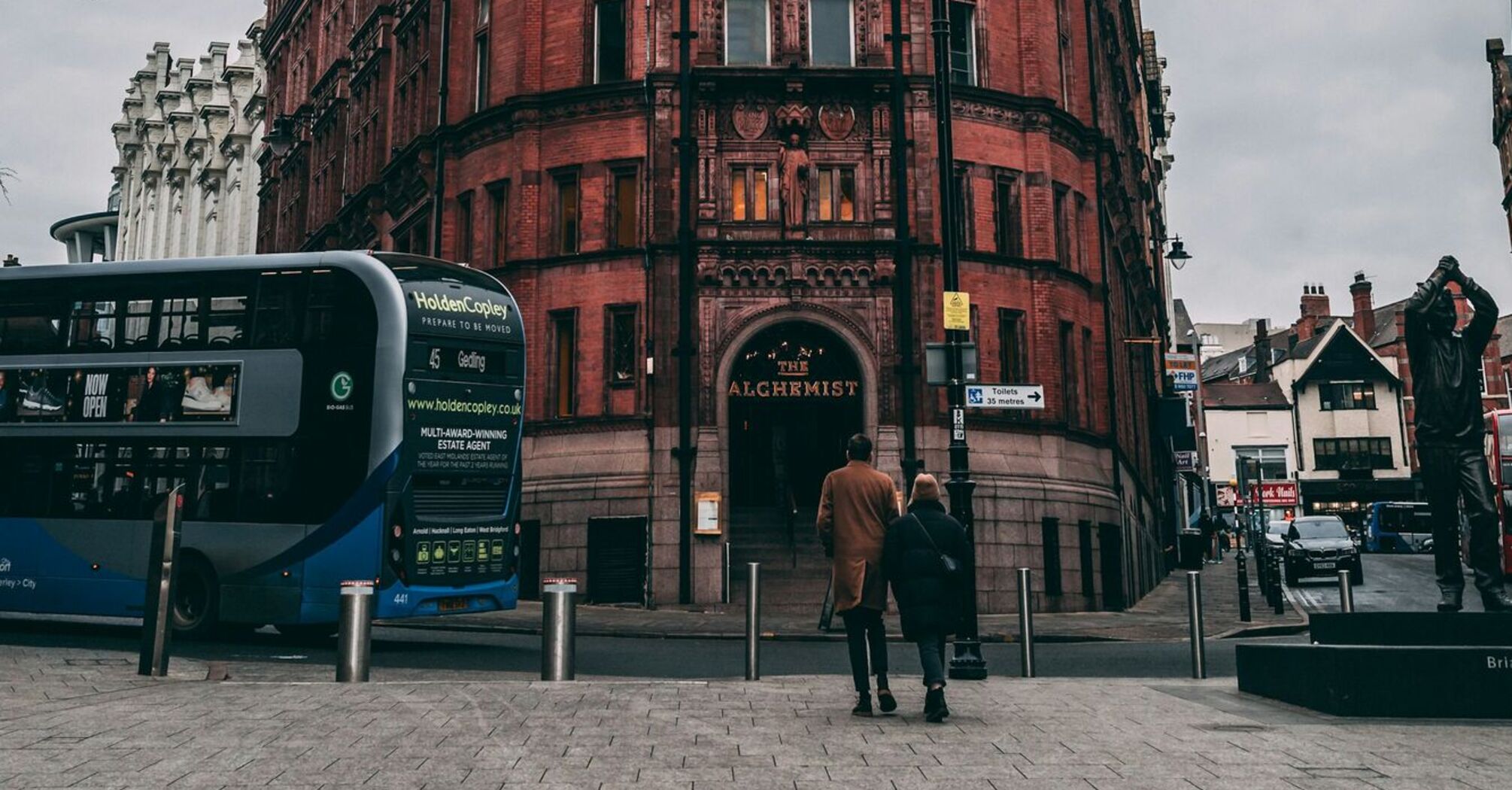 An old, red brick building in Nottingham with a bus and pedestrians in front