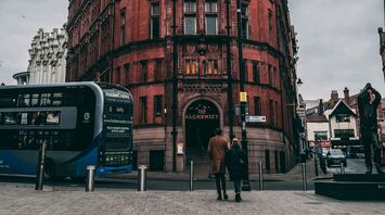 An old, red brick building in Nottingham with a bus and pedestrians in front