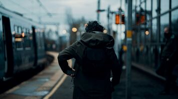 A person waiting on the platform at station with a train in the background