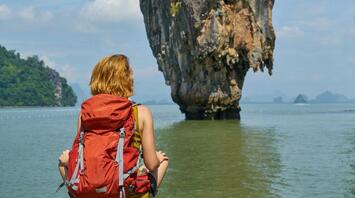 A tourist with a backpack sits in front of a famous rock