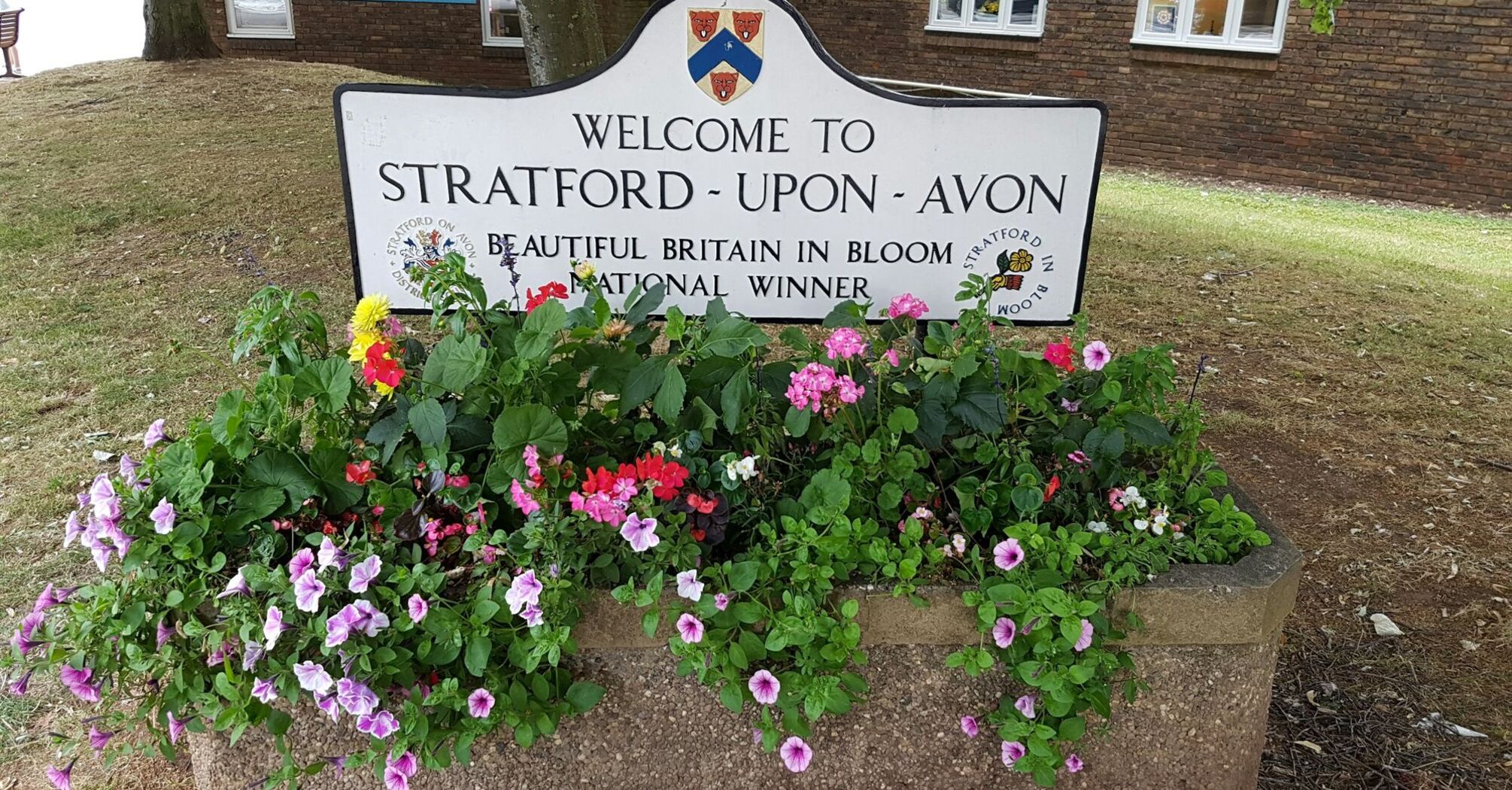 A "Welcome to Stratford-upon-Avon" sign with colorful flowers in front of the Visitor Information Centre