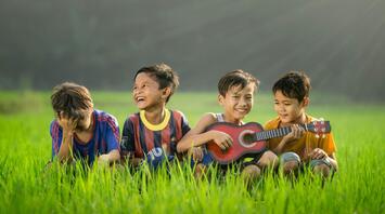 Four boys laugh on the grass, one plays the guitar