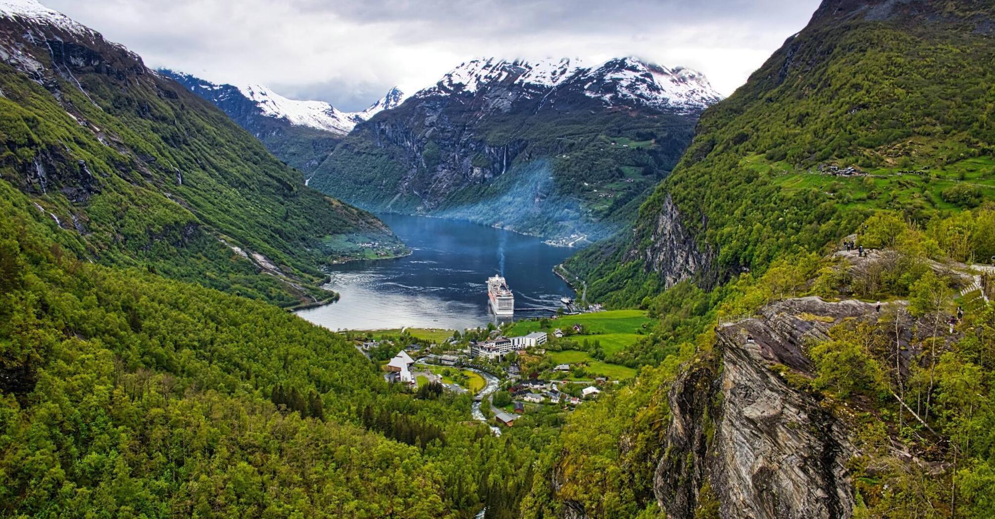 Cruise ship in a fjord surrounded by green and snowy mountains