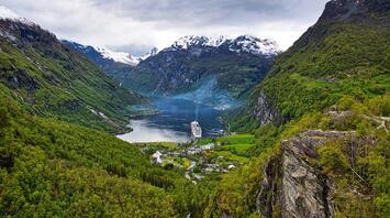 Cruise ship in a fjord surrounded by green and snowy mountains