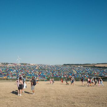 Festival goers walking towards a large campsite filled with colorful tents under a clear blue sky at Boardmasters