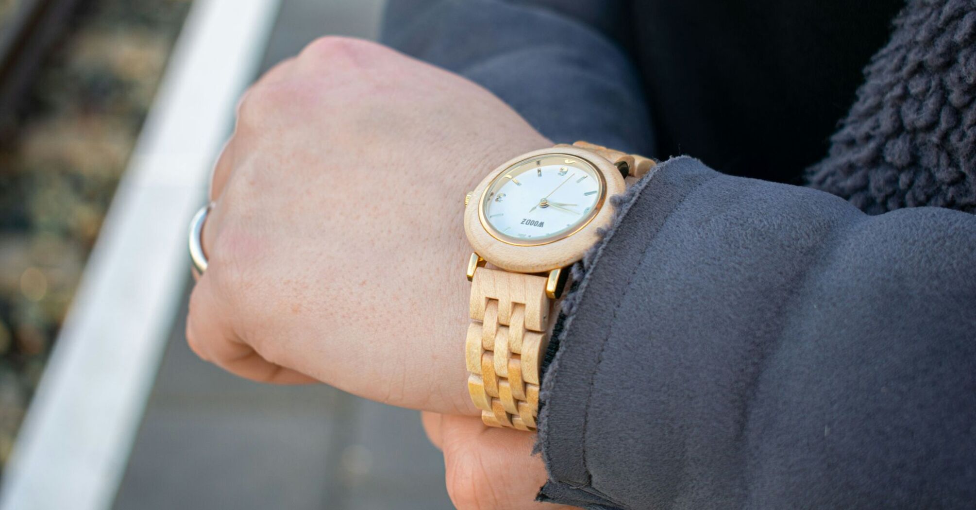 A close-up of a person checking the time on a wooden wristwatch while standing on a train platform