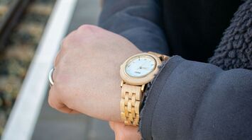 A close-up of a person checking the time on a wooden wristwatch while standing on a train platform