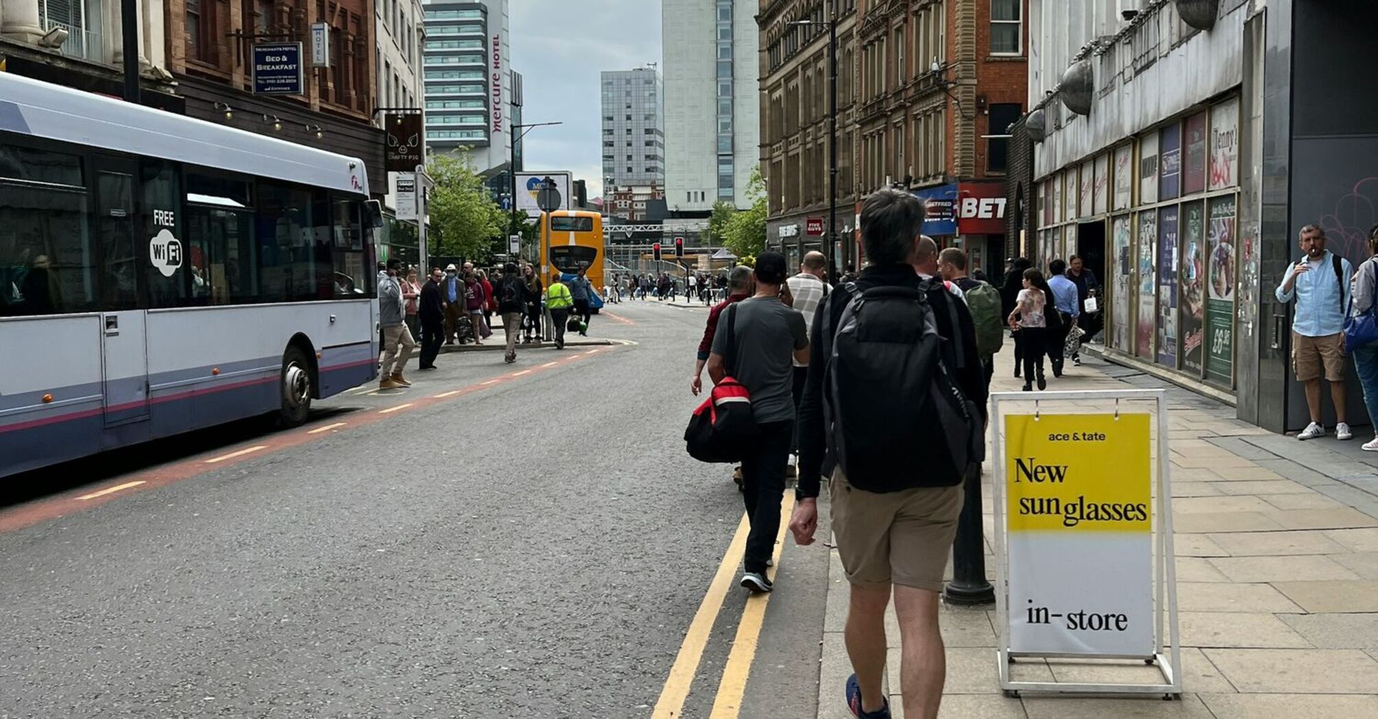 A bustling street in Manchester with buses and pedestrians, featuring historic and modern buildings