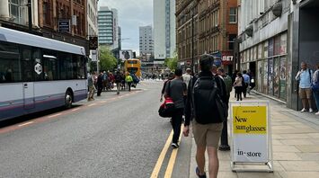 A bustling street in Manchester with buses and pedestrians, featuring historic and modern buildings