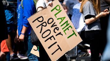 woman holding planet over profit placard