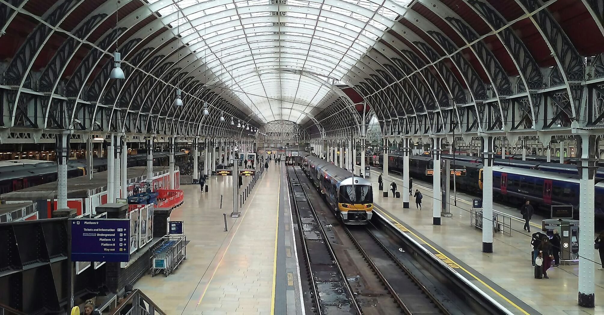 Interior view of a modern train station with a glass roof, showing platforms and trains ready for departure