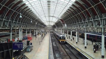 Interior view of a modern train station with a glass roof, showing platforms and trains ready for departure