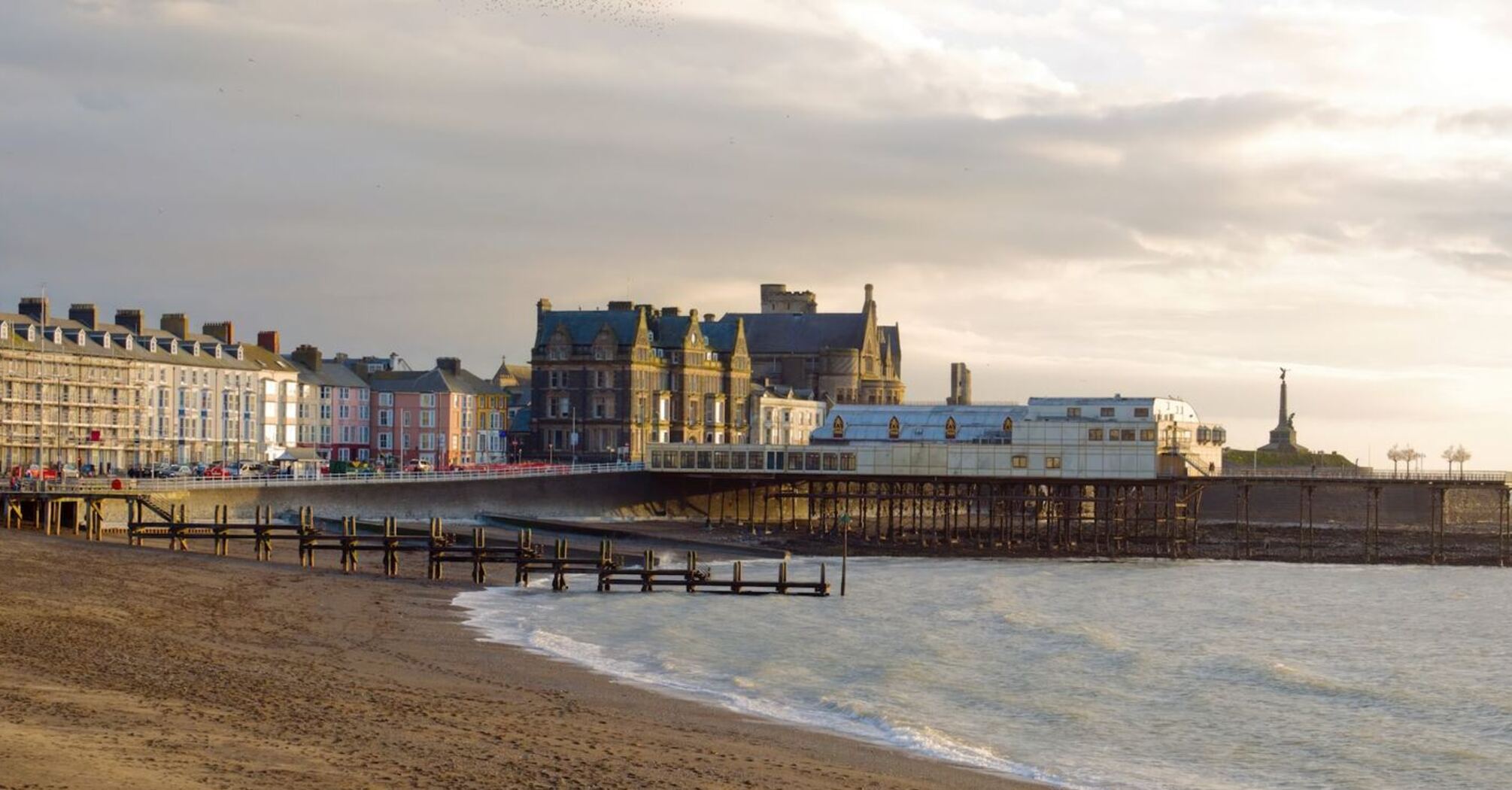 Scenic view of Aberystwyth coastline with historic buildings and a pier at sunset