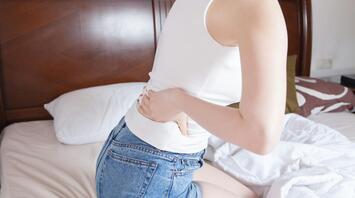 Woman sitting on bed holding her sore lower back