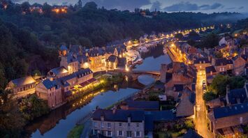 A picturesque evening view of a French village along a river, illuminated by street lights