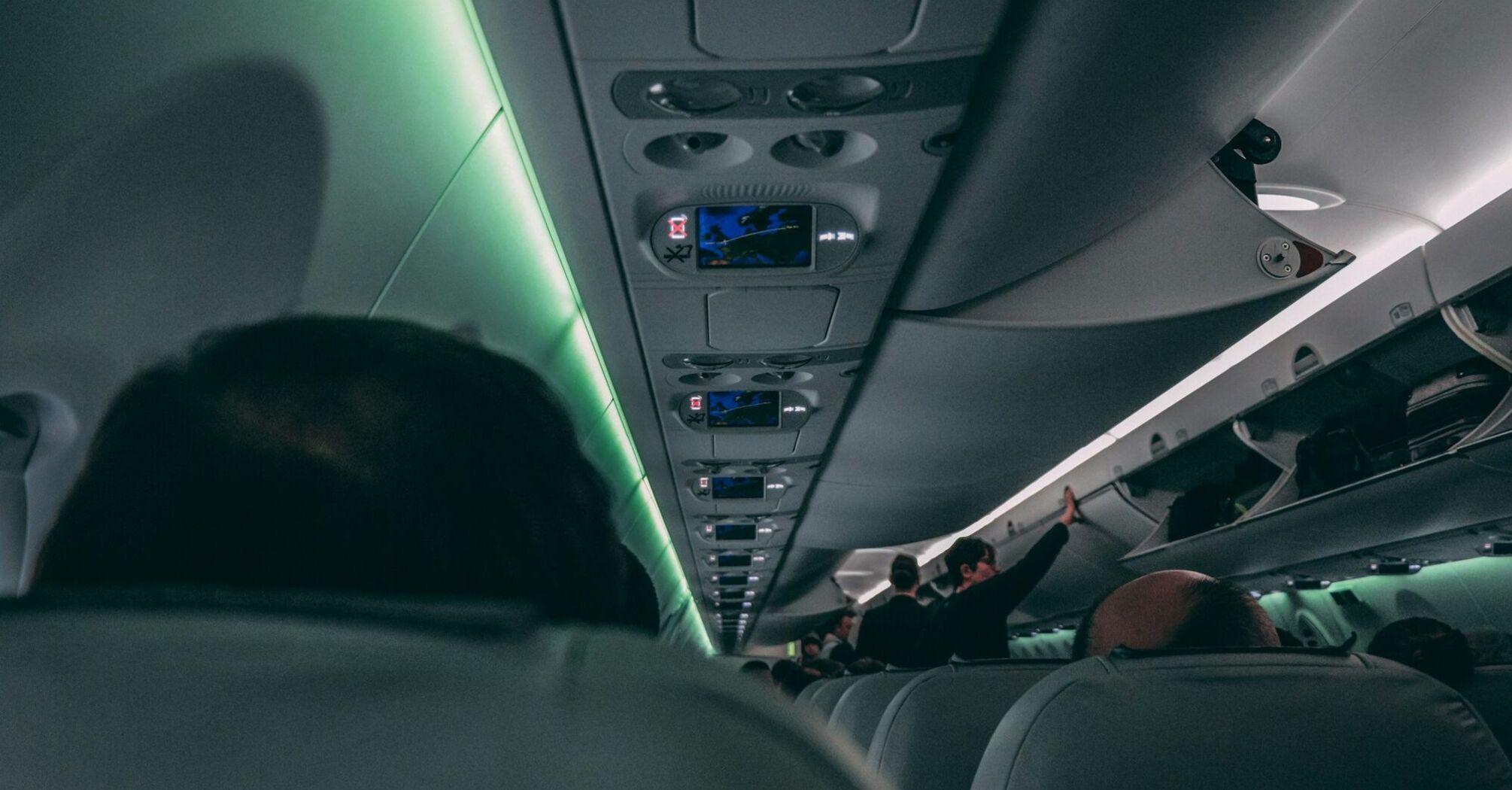 Inside view of an airplane cabin with passengers seated and flight attendants organizing overhead compartments