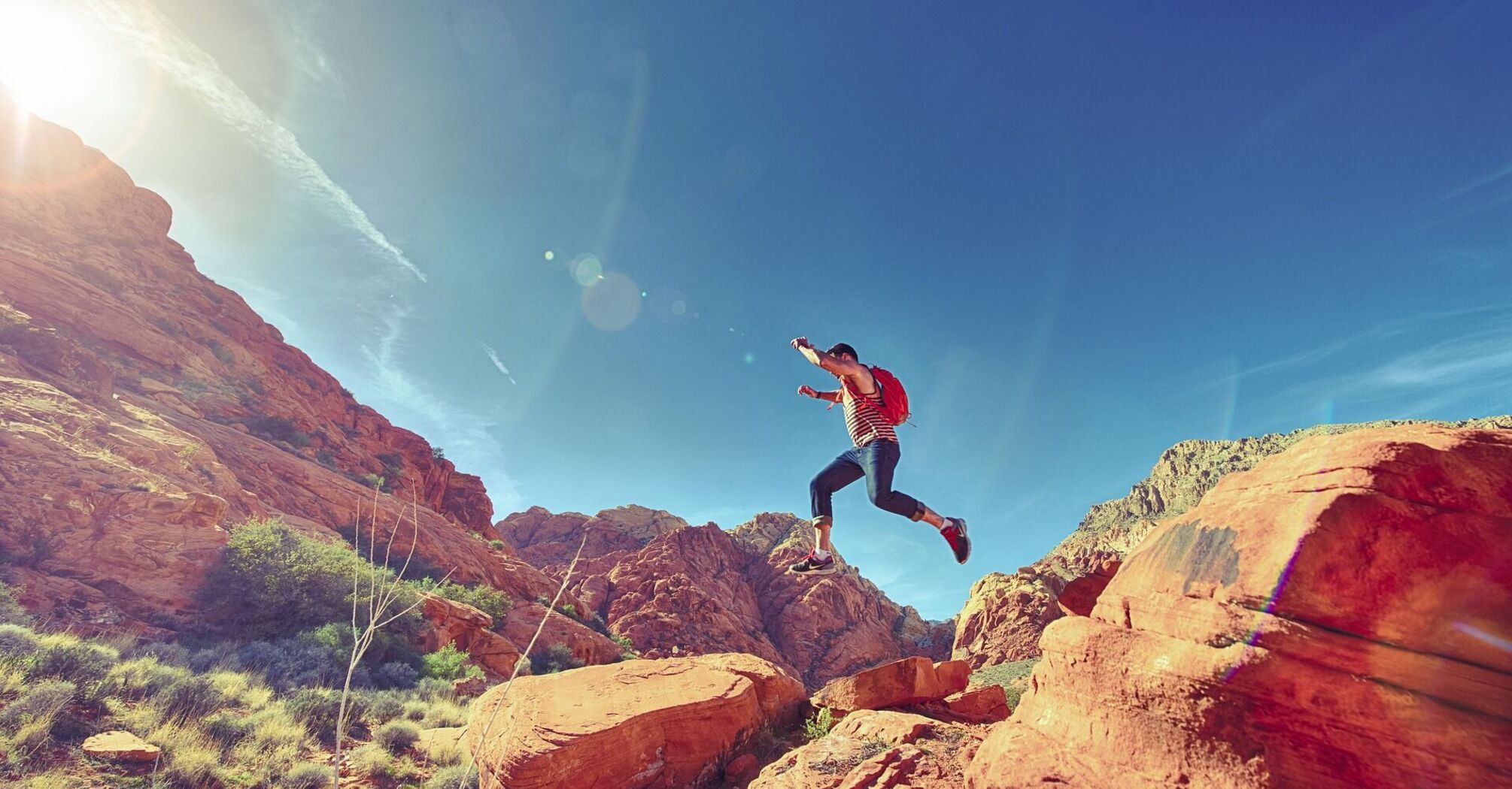 Person jumping between rocks in a sunny desert landscape