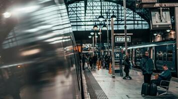A bustling train station with passengers waiting on the platform and a train reflected in the glass