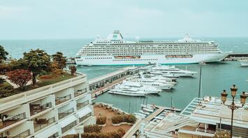 A large cruise liner docked at the port near a modern pier surrounded by yachts