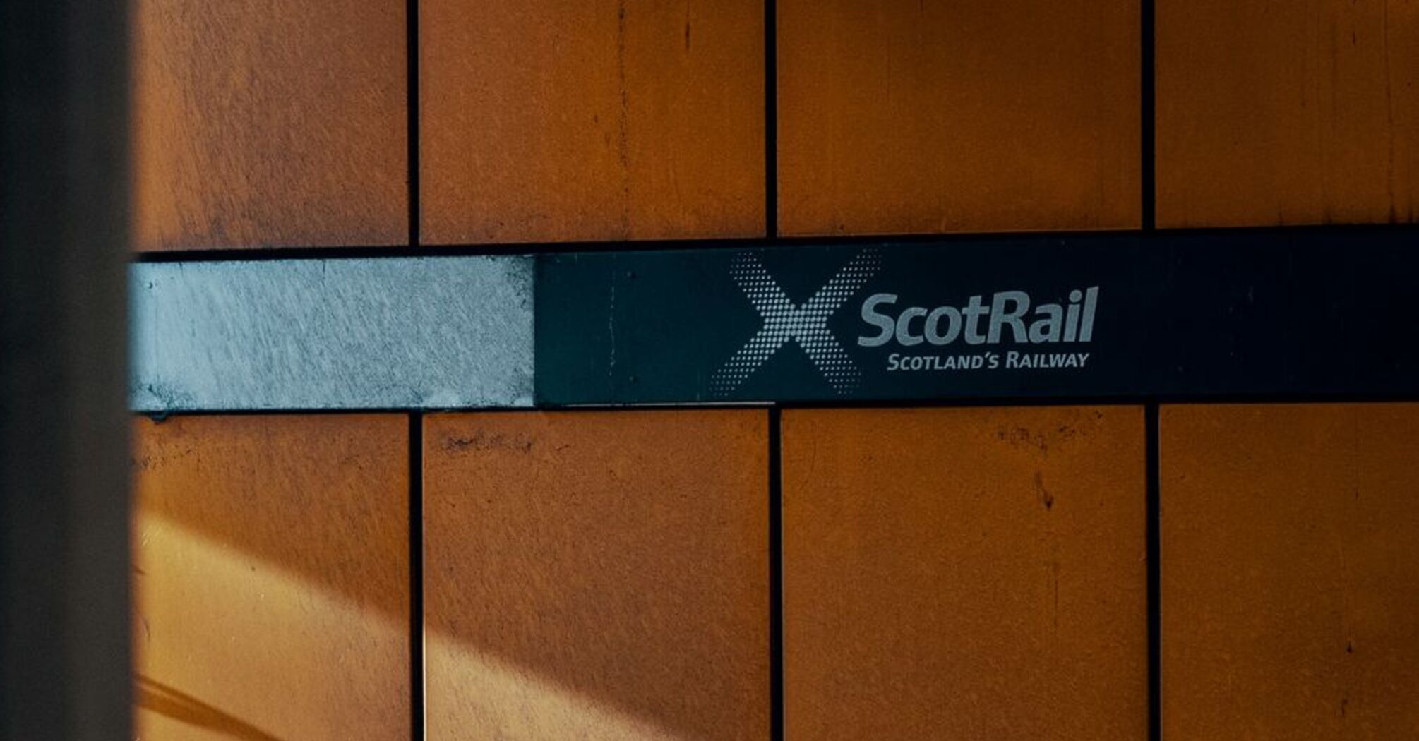 A Scotrail sign on a station wall, illuminated by sunlight