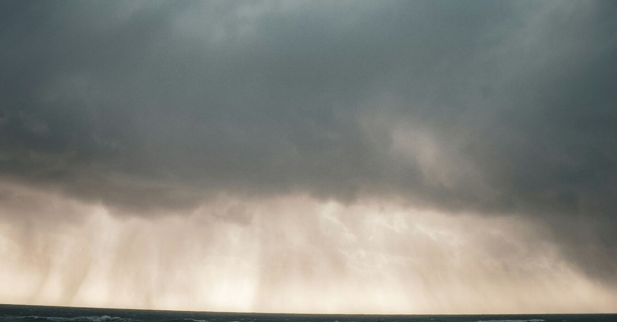 A dramatic sky with dark clouds and heavy rain over the sea, indicating stormy weather conditions